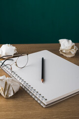 notebook with blank sheets on wooden table with crumpled paper balls, pencil and glasses
