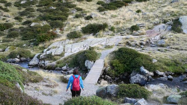Curvy young girl crossing the river on the wooden bridge during a hike in the mountains of Andorra dressed in sportswear