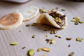 Piece of qatayef on wooden table stuffed with pistachio and chocolate