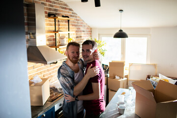 Male gay couple standing in new home looking at camera