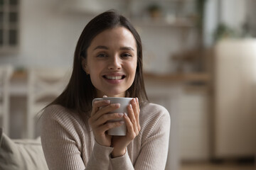 Portrait of beautiful young woman holding teacup sitting alone at home smile looks at camera....