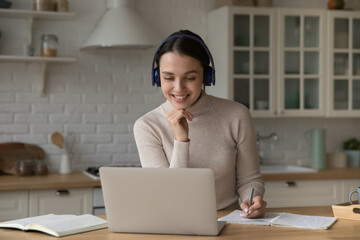 Student woman in headphones studying at home using laptop, writing essay, prepare assignment, make...
