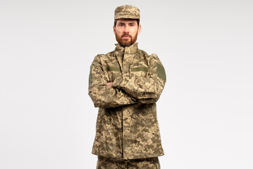 Handsome serious bearded man, professional soldier wearing camouflage military uniform holding arms crossed isolated on white background  