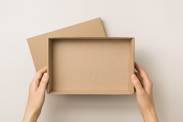 female hands holding an empty brown kraft box on a gray background, top view. delivery concept