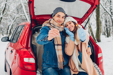 Young couple in love burning sparklers in car trunk in snowy winter forest. People relaxing during Christmas season