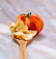 Pasta placed on a wooden spoon and tomato cut in two, macro