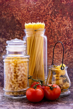Different pastas put in glass jars and tomatoes