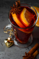 A glass of glitwine, with spices cinnamon and star anise, orange, New Year's decor in the shape of a heart on a dark background, close up.