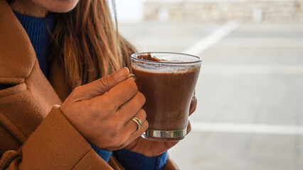 Person drinking hot chocolate in cafe. Closeup of female hands holding a cup