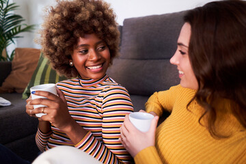 Close up of two woman talking in the living room drinking coffee and talking cheerfully in the...