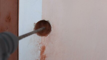 A man drills a hole in a brick wall using a hammer drill and a long drill. Home repairs. Video with sound.
