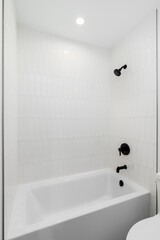A shower and bathtub with white picket tiles and black faucet and showerhead.