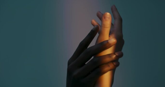 White female hands and dar skinned man's hand together touching each ther dancing against the bright light in dark studio .