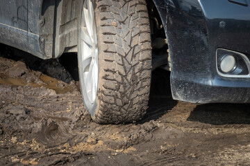 Winter car tires are covered with mud, the car is in the mud. Tough road conditions highlight the...