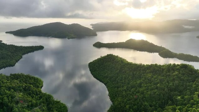 Low, sunlit clouds drift across the scenic island of Batanta in Raja Ampat, Indonesia, at dawn. This area is known as the heart of the Coral Triangle due to its incredibly high marine biodiversity.
