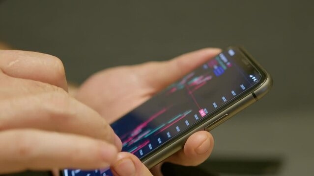 Stock market candlestick chart view on the phone in hands of a man in front of monitor with chart. High quality 4k footage