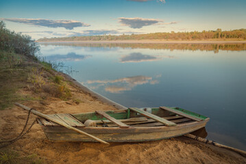 An old wooden boat is moored on the sandy bank of the river.