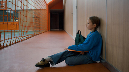 Unhappy little girl sitting floor gym tired primary school lesson schoolgirl fatigue weary child...