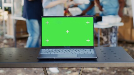 Close-up of electronic laptop with isolated green screen sits on a table while charity workers...