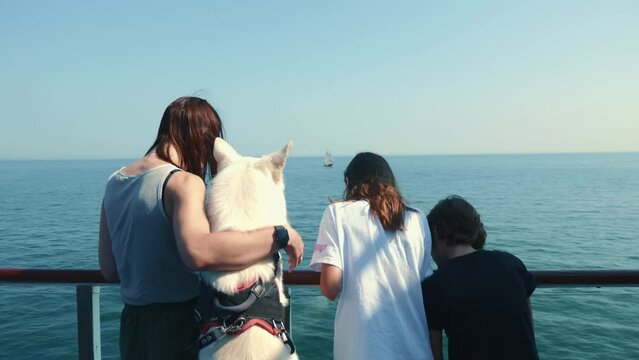 Young woman, teenage girl and boy and white shepherd dog enjoying the sea view from the ferry together.