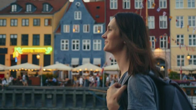 Attractive happy young woman walking in front of the famous colorful houses and smiling in Nyhavn, Copenhagen