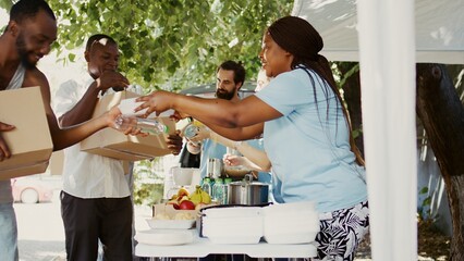 In a sunny day, multiethnic volunteers distribute donations of food to the needy, offering help and...