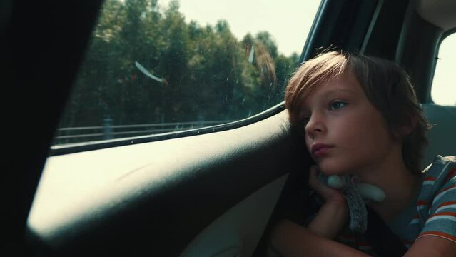 Thoughtful young teenage boy stares out the car window at the view passing by