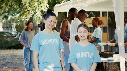 Portrait shot of mother and daughter participating in hunger relief program at outdoor food bank....