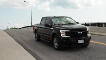 top of large big bridge road with cars vehicles traffic coming and going passing zooming uphill downhill ascending descending with sidewalk and railing and clouds sky behind