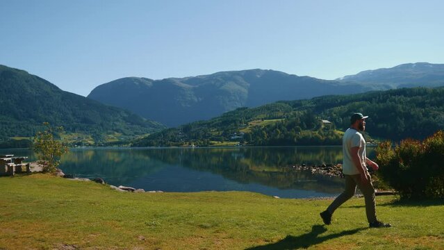 Young handsome man walking with stunning mountain lake landscape in the background on a sunny day.