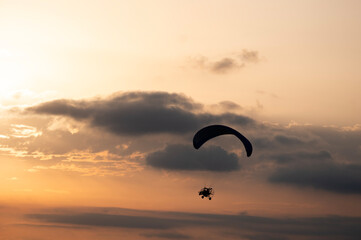 Fototapeta na wymiar Paramotor tandem flying silhouette in the golden hours with nice clouds on a summer evening