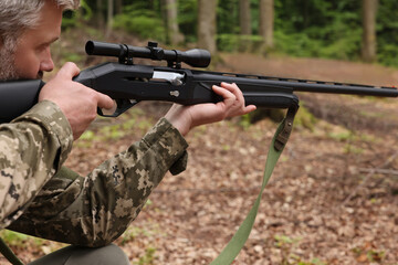 Man wearing camouflage and aiming with hunting rifle in forest, closeup