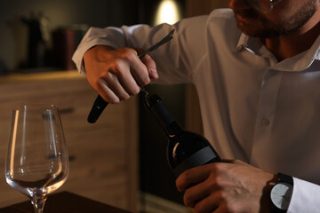 Romantic dinner. Man opening wine bottle with corkscrew indoors, closeup