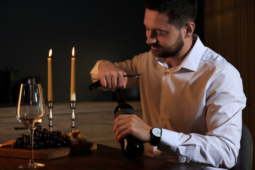 Romantic dinner. Man opening wine bottle with corkscrew at table indoors