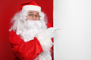 Santa Claus pointing at blank poster on red background, space for text