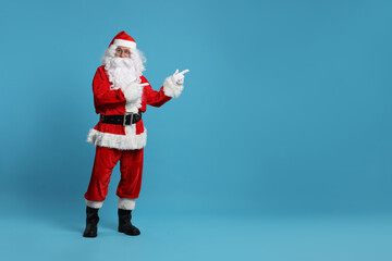 Merry Christmas. Santa Claus pointing at something on light blue background, space for text