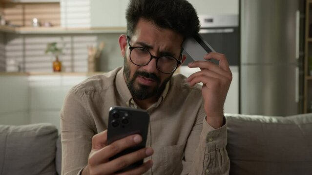 Stressed Arabian Indian man frustrated upset male cardholder pay online service with bank credit card using mobile phone disappointed banking app error no money balance lack finances financial limit
