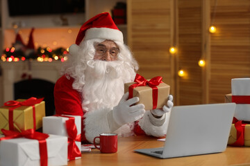 Santa Claus with Christmas gift using laptop at table in room
