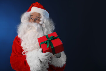 Santa Claus with Christmas gift on dark blue background. Space for text
