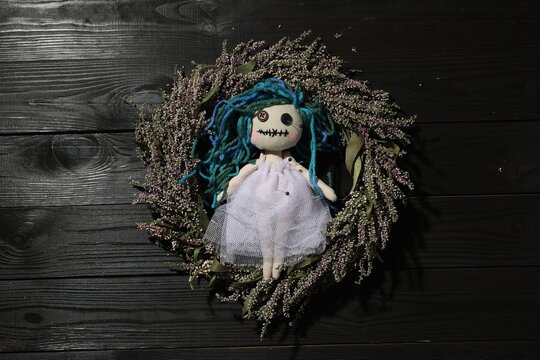Female voodoo doll with pins and wreath on black wooden background, top view