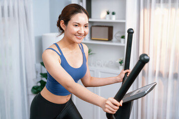 Energetic and strong athletic asian woman running on elliptical running machine at home. Pursuit of...