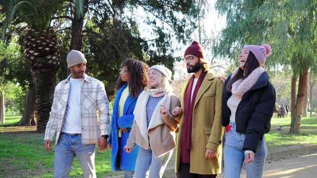 Slow motion fotage of a group of international best friends walking and talking at downtown park, smiling and laughing together. Happy young adult people sightseeing with autumnal or wintry clothes