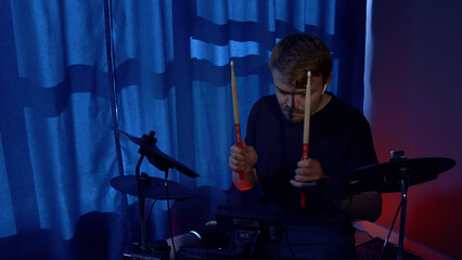 Fototapeta premium Young musician drummer playing drums with drumsticks at sound studio. Media. Man drumming with sticks during rehearsal.