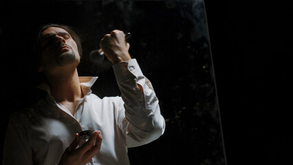Male reflection in a dark room. Stock footage. Man actor powdering his face.