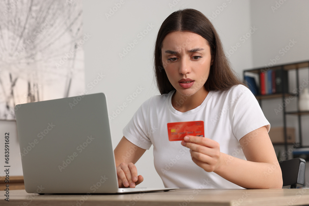 Canvas Prints Confused woman with credit card using laptop at table indoors. Be careful - fraud