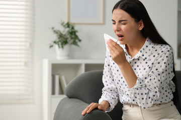 Suffering from allergy. Young woman with tissue sneezing at home, space for text