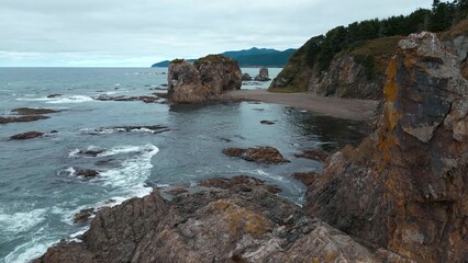 Top view of rocky coast with cliffs. Clip. Cinematic landscape with northern coast and cliffs. Rocky northern shore with green forests on cloudy day