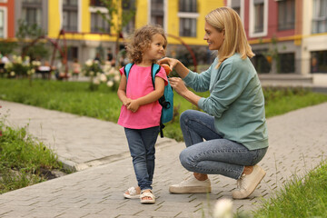 Happy mother putting apple into with her daughter's backpack near kindergarten outdoors
