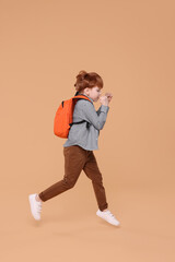 Cute schoolboy with backpack running on beige background