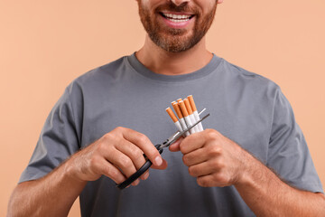 Stop smoking concept. Man cutting cigarettes on light brown background, closeup